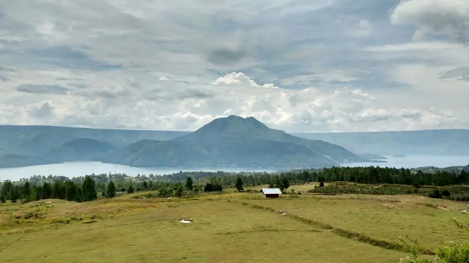Suasana dermaga kecil di tepi Danau Toba dengan perahu biru dan latar bukit hijau
